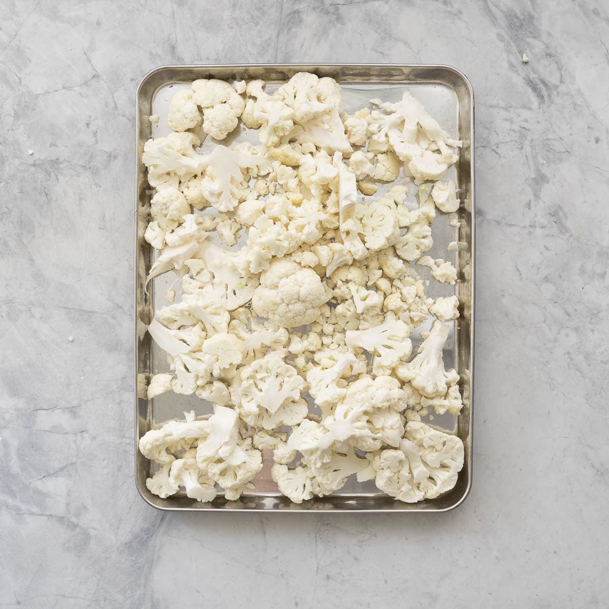 Cauliflower pieces broken on a lined tray with baking paper on bench top.