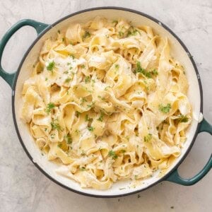 Cauliflower alfredo sauce mixed through cooked pasta topped with chopped parsley in a ceramic dutch oven pan on benchtop.