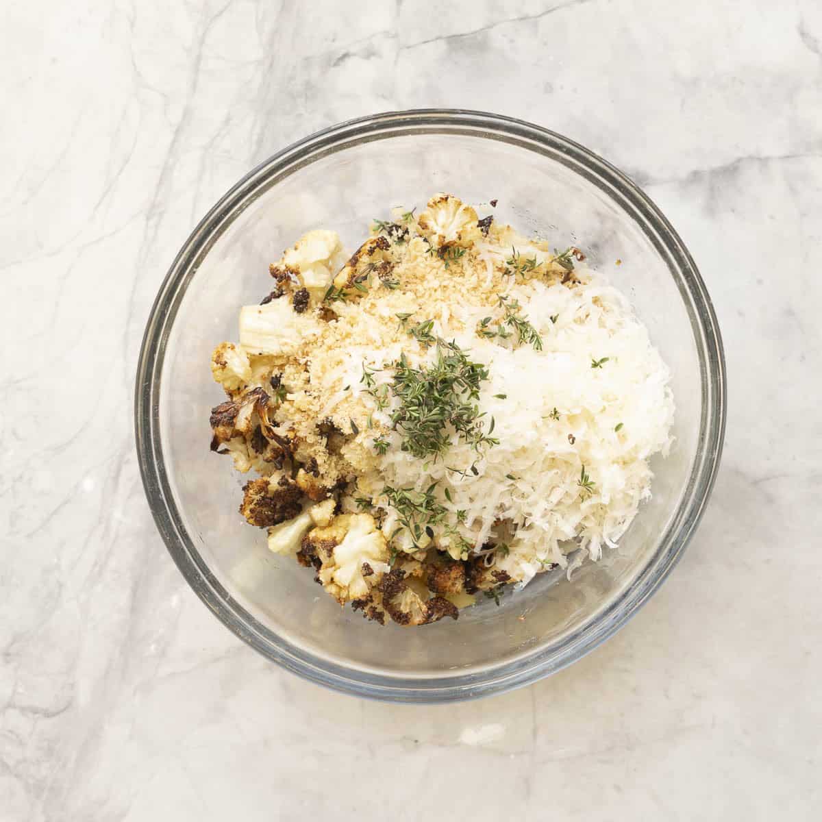 Crispy roasted cauliflower, panko bread crumbs, thyme and parmesan cheese in a glass bowl on benchtop.
