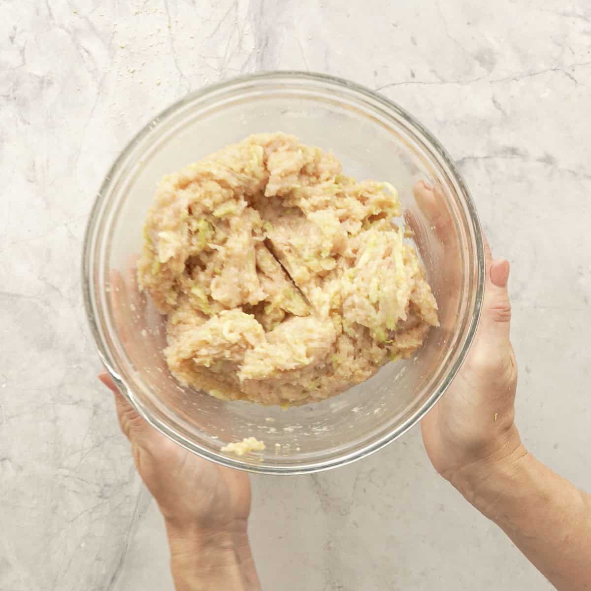 Hands holding Chicken meatball mixture mixed together in a glass bowl.