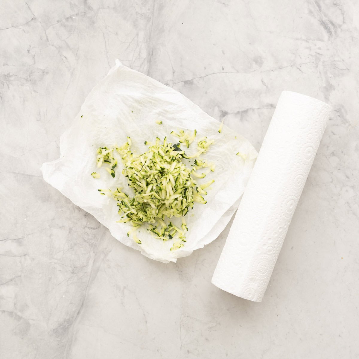Grated Zucchini on paper towel on benchtop.