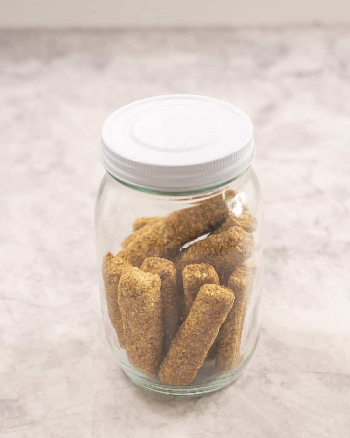 Jar of baby rusks with lid on sitting on benchtop.