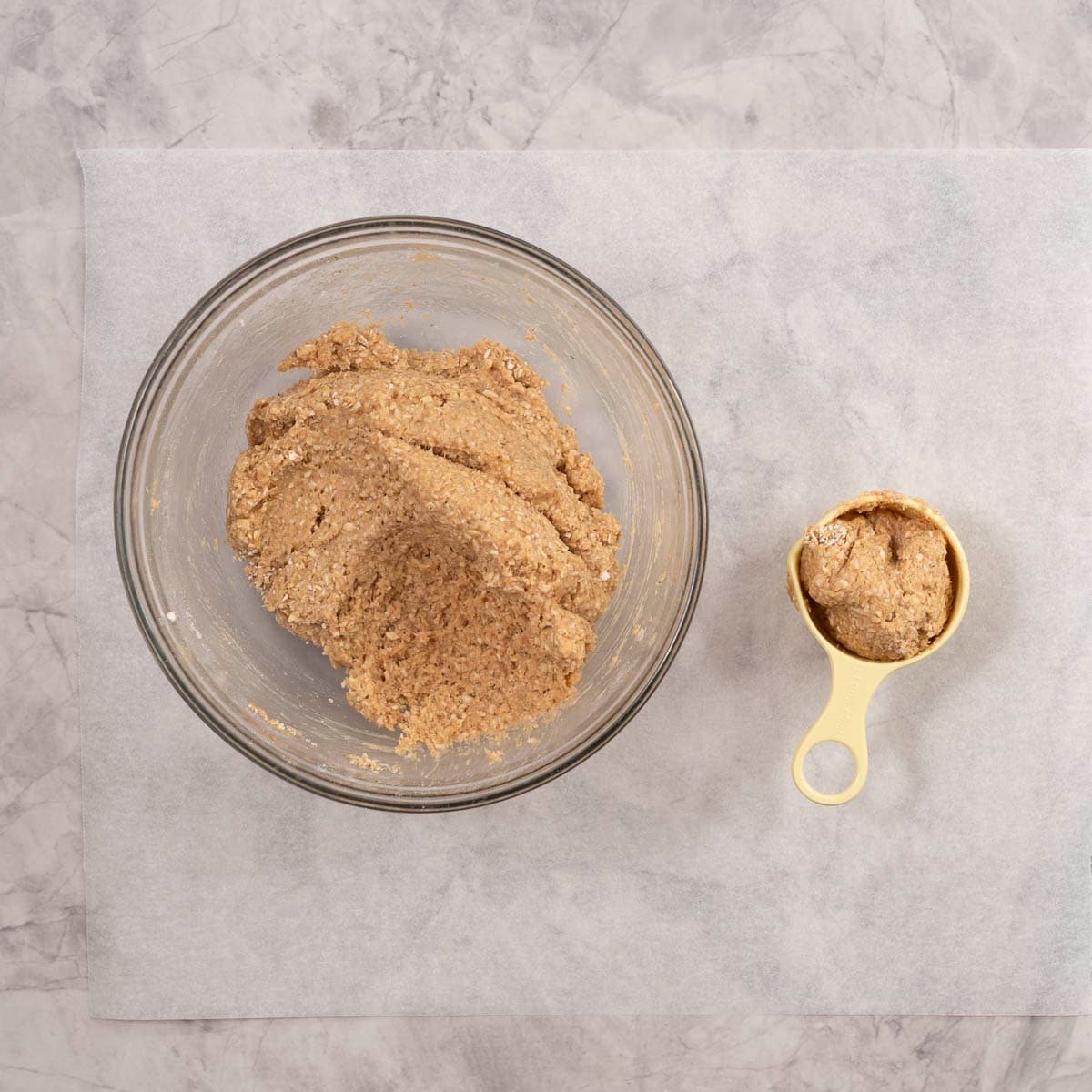 Baby rusk mixture in a large glass bowl, measuring cup with mixture inside.