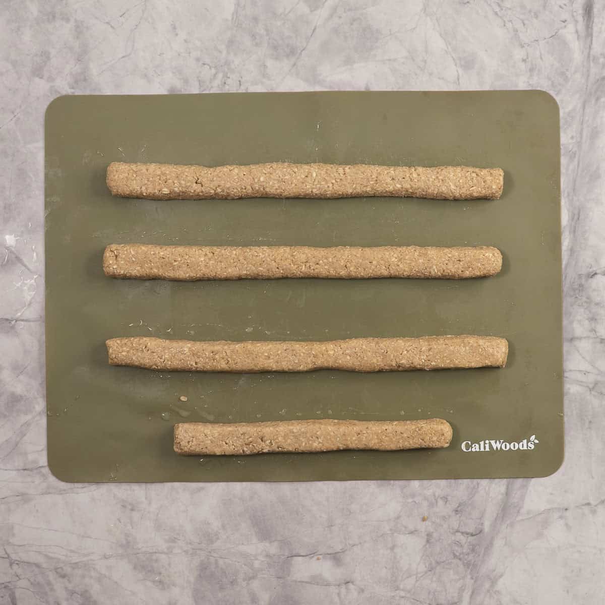 Uncooked baby rusks on silicone baking mat rolled into 4 long strips with squared edges.