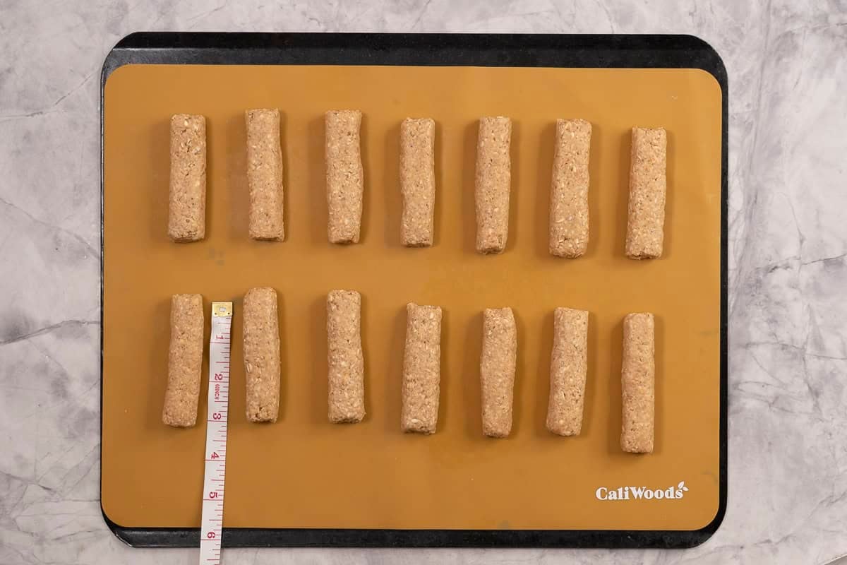 Lined baking tray with baby rusks in two rows spaced apart, measuring tape next to a rusk showing