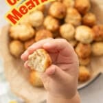 A toddler hand lifting a partially eaten chicken meatball up to the camera with text overlay: Chicken Meatballs, loved by all ages.