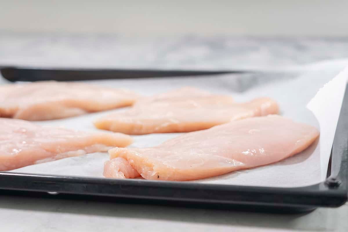 Chicken breasts on lined baking tray.