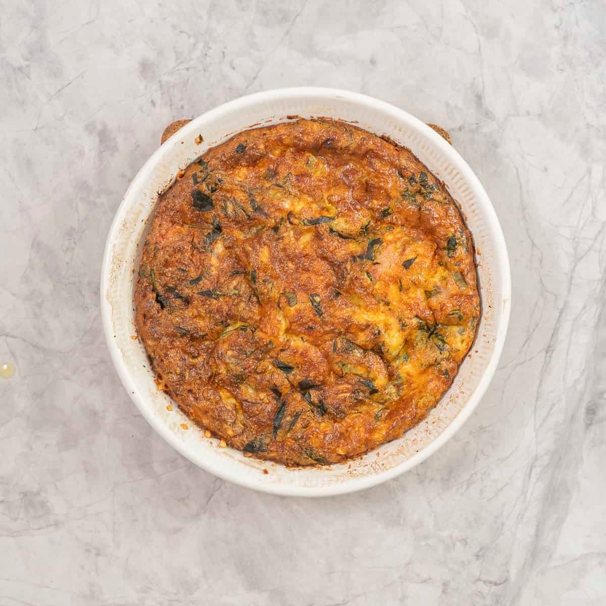 Cooked cuiche slightly golden on top in a round baking dish on benchtop.