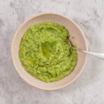 Mashed peas in a bowl with spoon garnished with piece of parsley and cracked pepper.