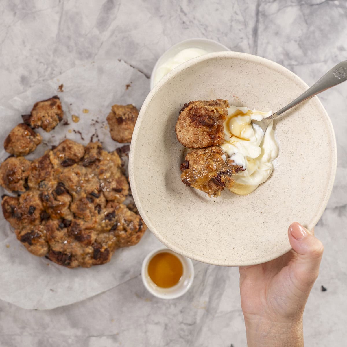 Cooked monkey bread on a piece of baking paper on bench top, desert bowl with yogurt and chopped banana served with monkey bread.