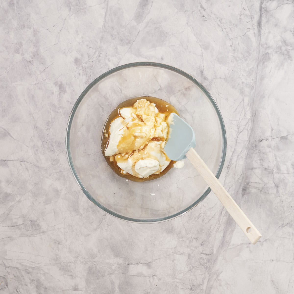 Yogurt, maple syrup and vanilla in a large glass bowl with spatula inside.
