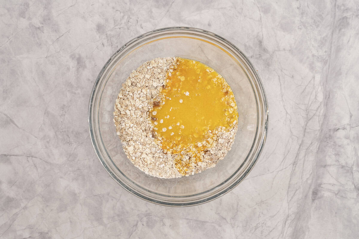 Wet ingredients poured into dry ingredients in glass bowl on benchtop.