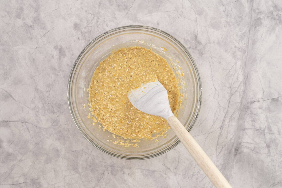 Wet and dry ingredients mixed together in large glass bowl with spatula inside.