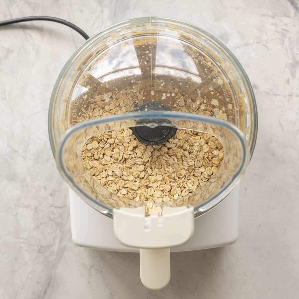 Apple sauce, peanut butter, raisins and oats in a food processor with lid on on benchtop.