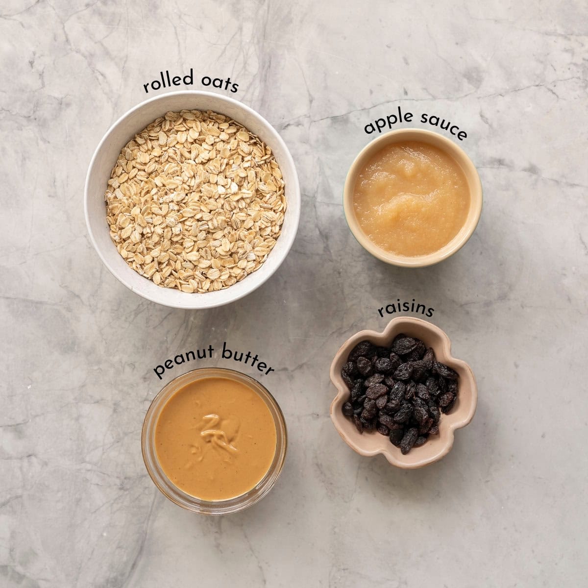 Ingredients for peanut butter oat balls on bench top in small ramekins on bench top.