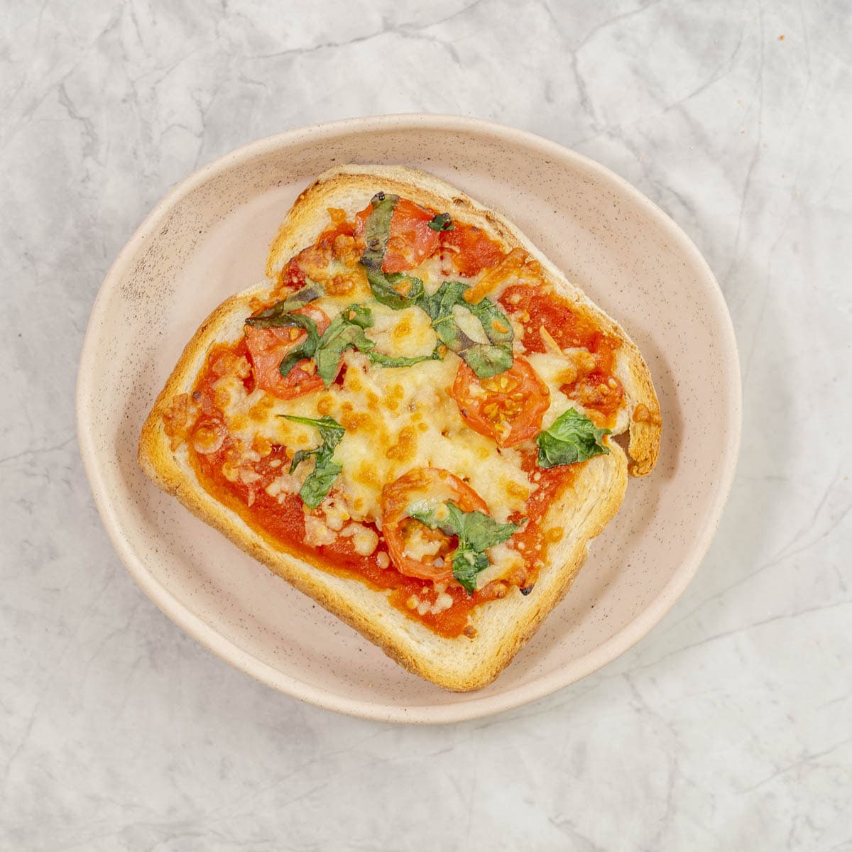 A slice of toast turned into pizza on a pink side plate.