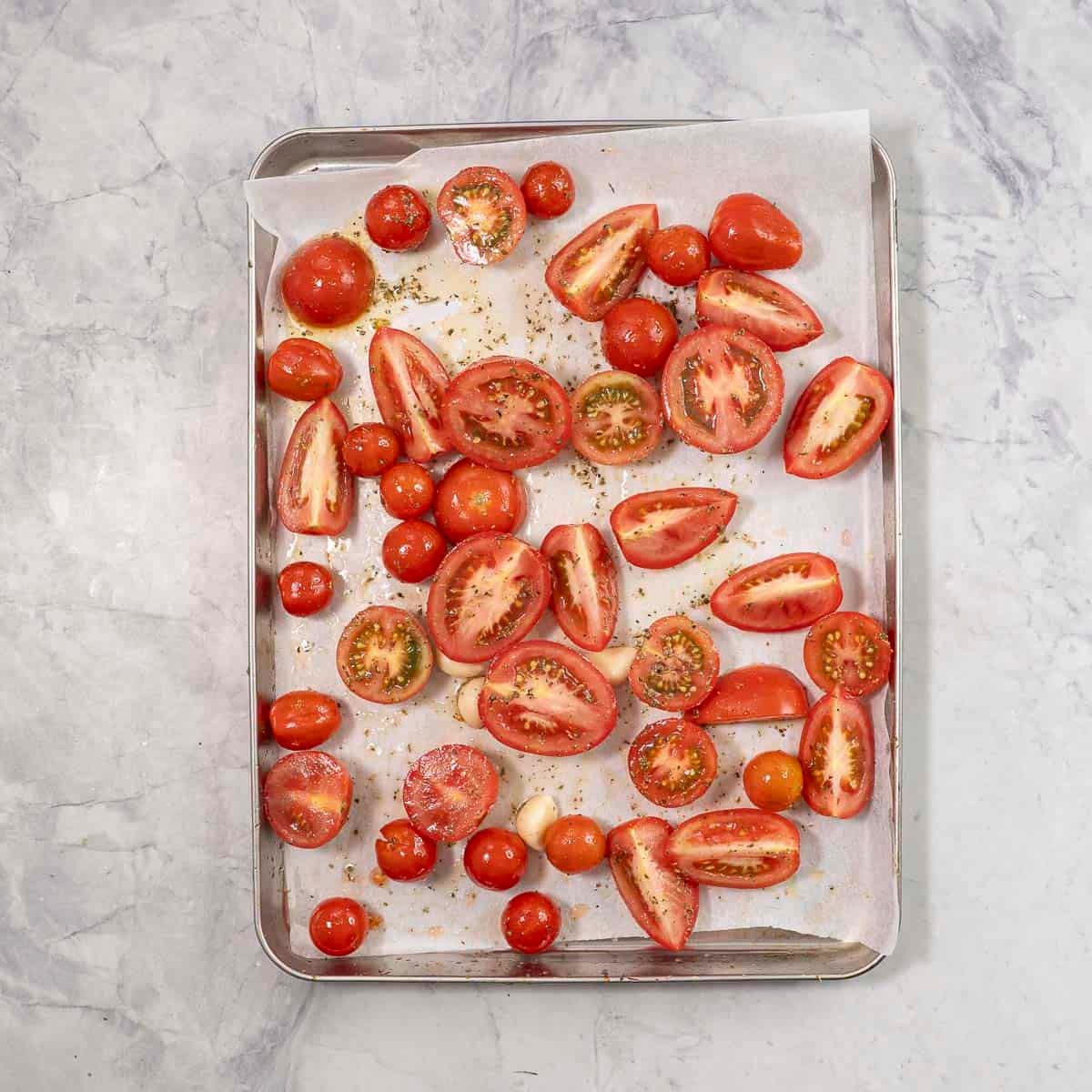 Chopped tomatoes on a lined baking tray seasoned.