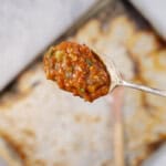Spoon with roasted tomato sauce held above lined baking tray.