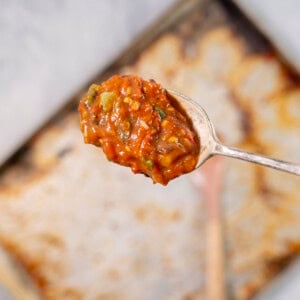 Spoon with roasted tomato sauce held above lined baking tray.