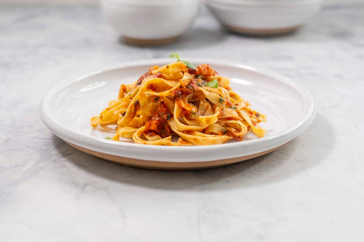Pasta and roasted tomato sauce mixed together on a dinner plate, topped with basil leaves.