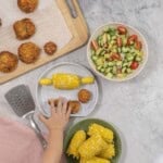 A marble coloured silicone baby plate with half a corn cob (corn handles inserted each end and 3 small fish cakes.