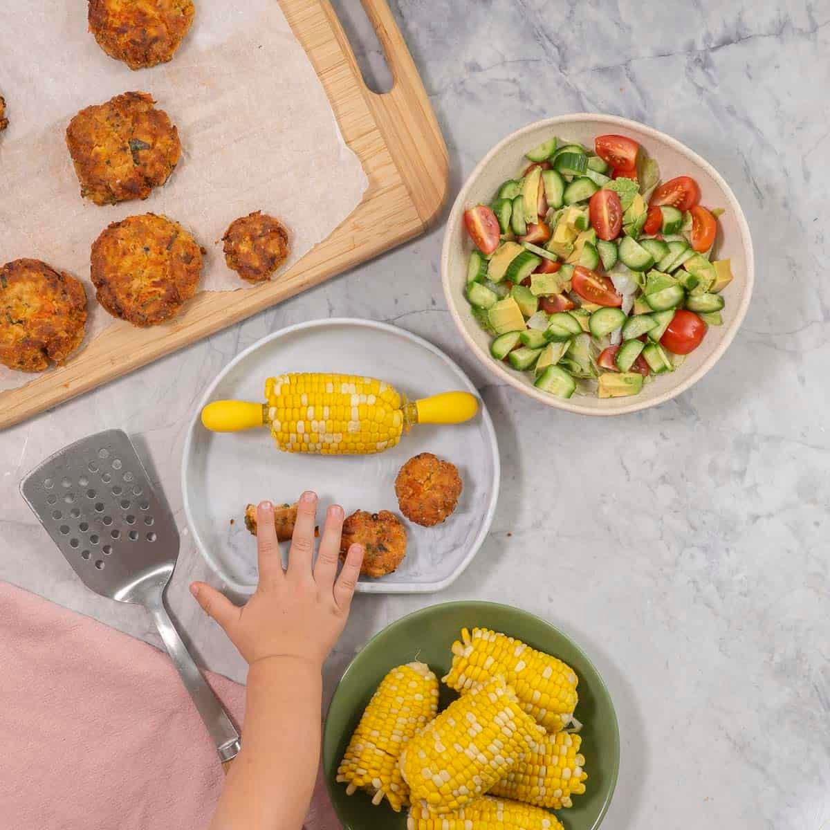 A marble coloured silicone baby plate with half a corn cob (corn handles inserted each end and 3 small fish cakes.