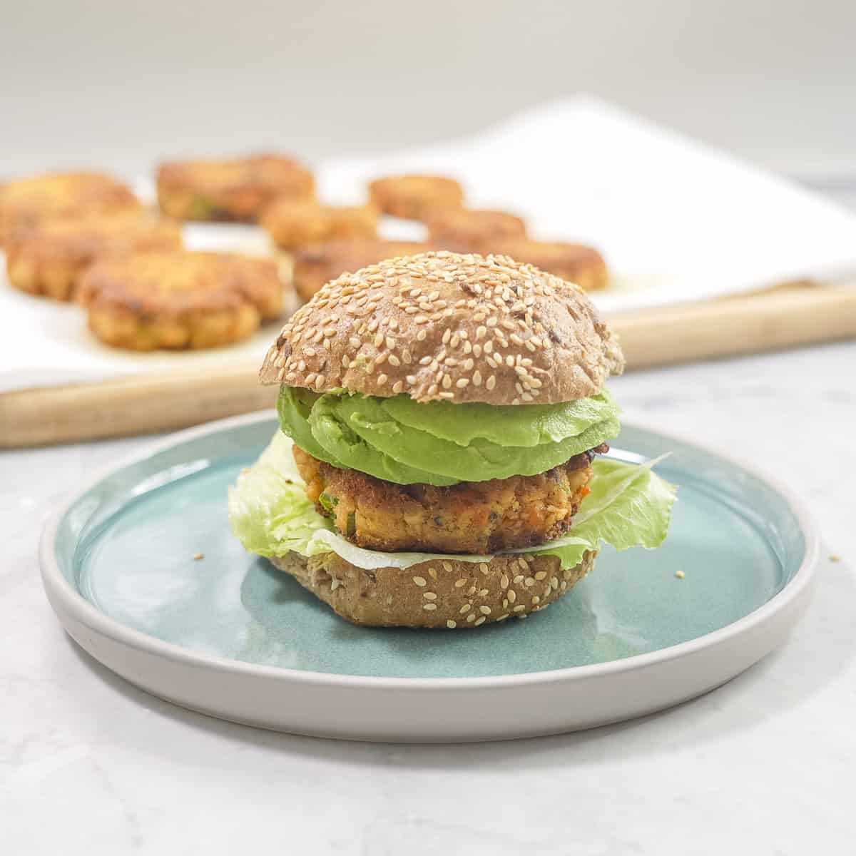 Burger buns with salmon pattie, lettuce inside on a blue plate on bench top.