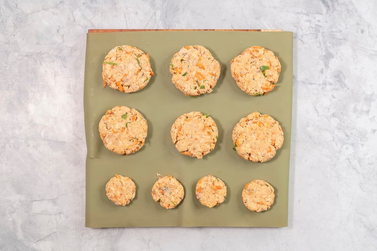 Six large salmon patties and four small patties on a silicone baking liner on bench top.