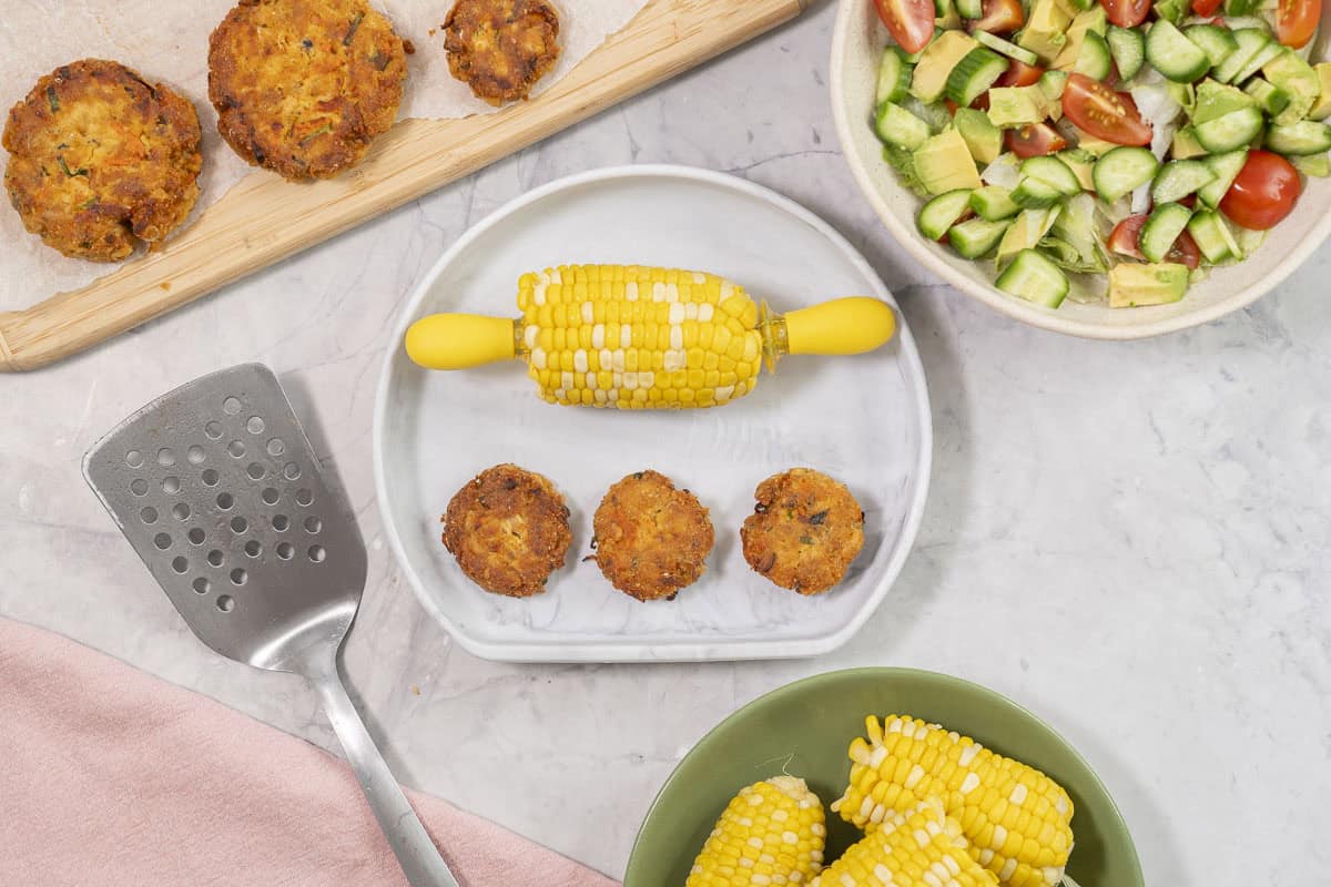 A marble coloured silicone baby plate with half a corn cob (corn handles inserted each end and 3 small fish cakes.