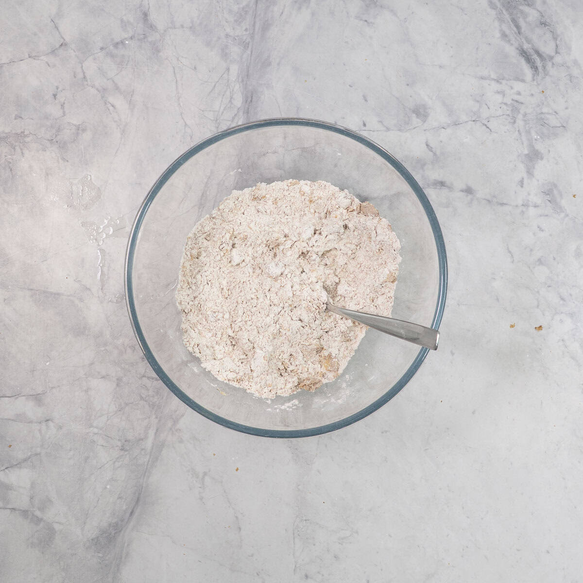 Glass bowl with dry ingredients and fork inside on benchtop.