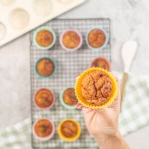 Hand holding a weebix muffin in yellow silicone mold above cooling tray with rest of muffins below.