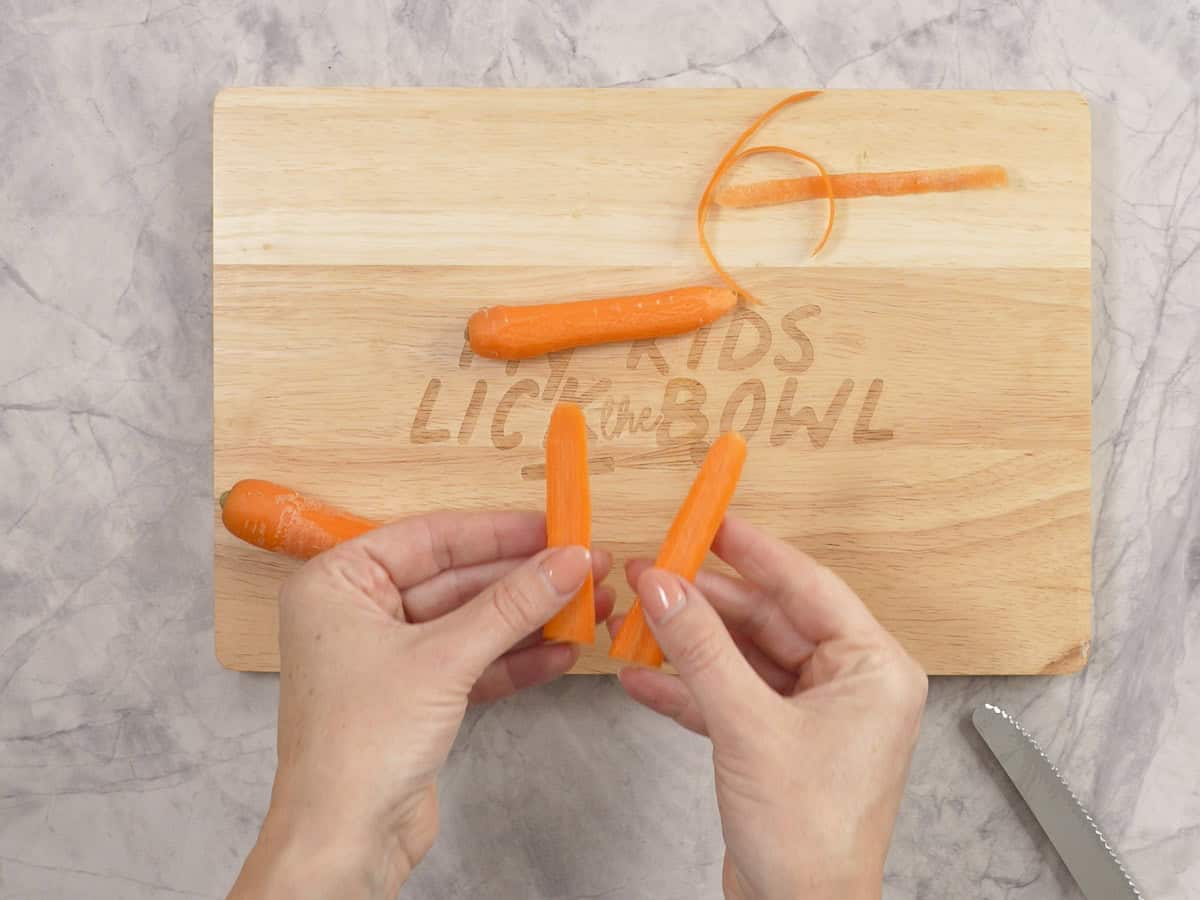 Womans hands holding two pieces of carrot cut to look in the shape of bunny ears.