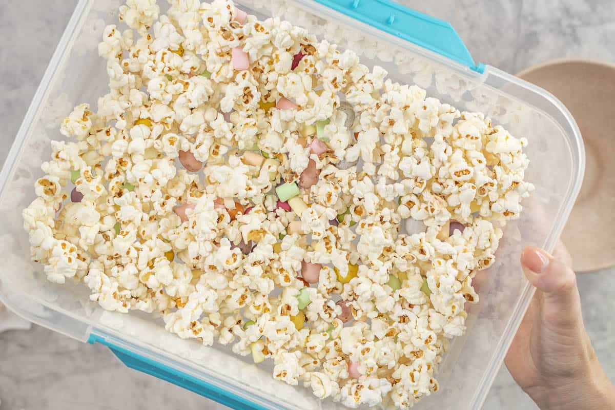 Womans hand holding a large container of popcorn with lollies scattered throughout.