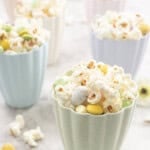 6 pastal coloured tall bowls filled with easter popcorn on benchtop.