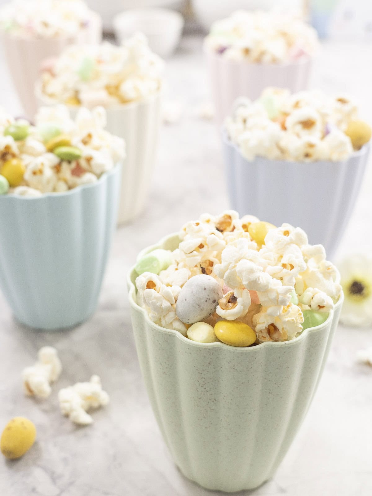 6 pastal coloured tall bowls filled with easter popcorn on benchtop.