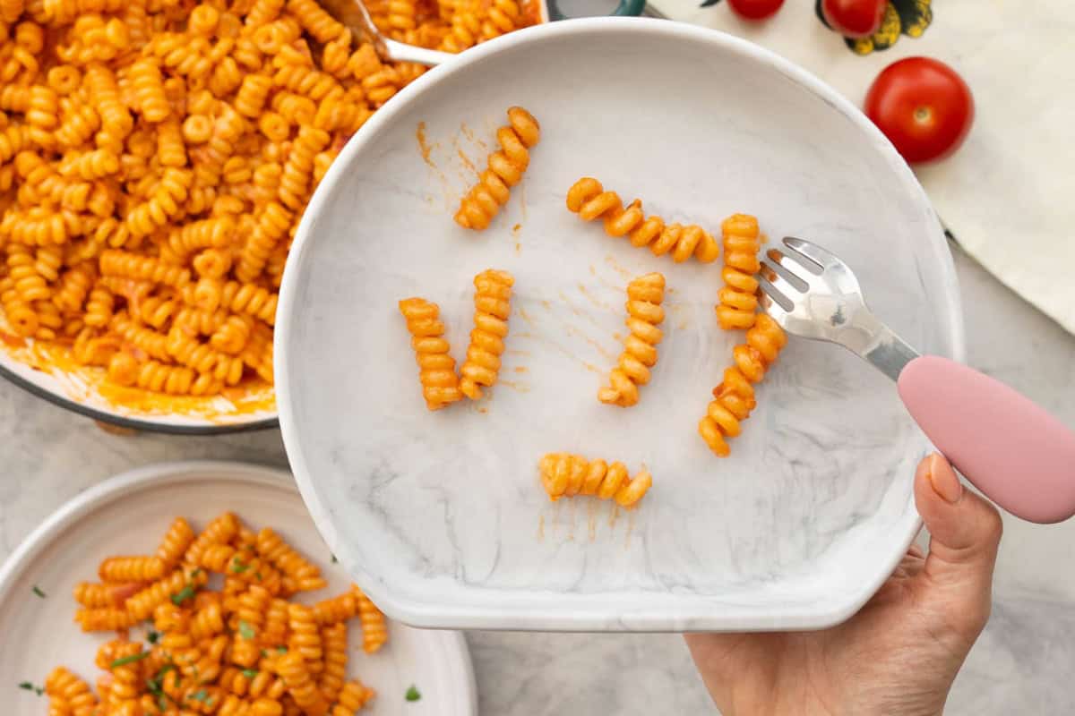 A baby plate with large pasta spirals coated in red pasta sauce.