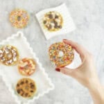 Womans hand holding a red apple with core removed sliced to look like a donut, spread with peanut butter and topped with sprinkles. 5 other apple donuts below with various toppings.