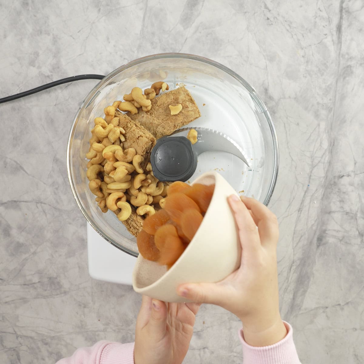 Toddler pouring a bowl of apricots into a food processor.