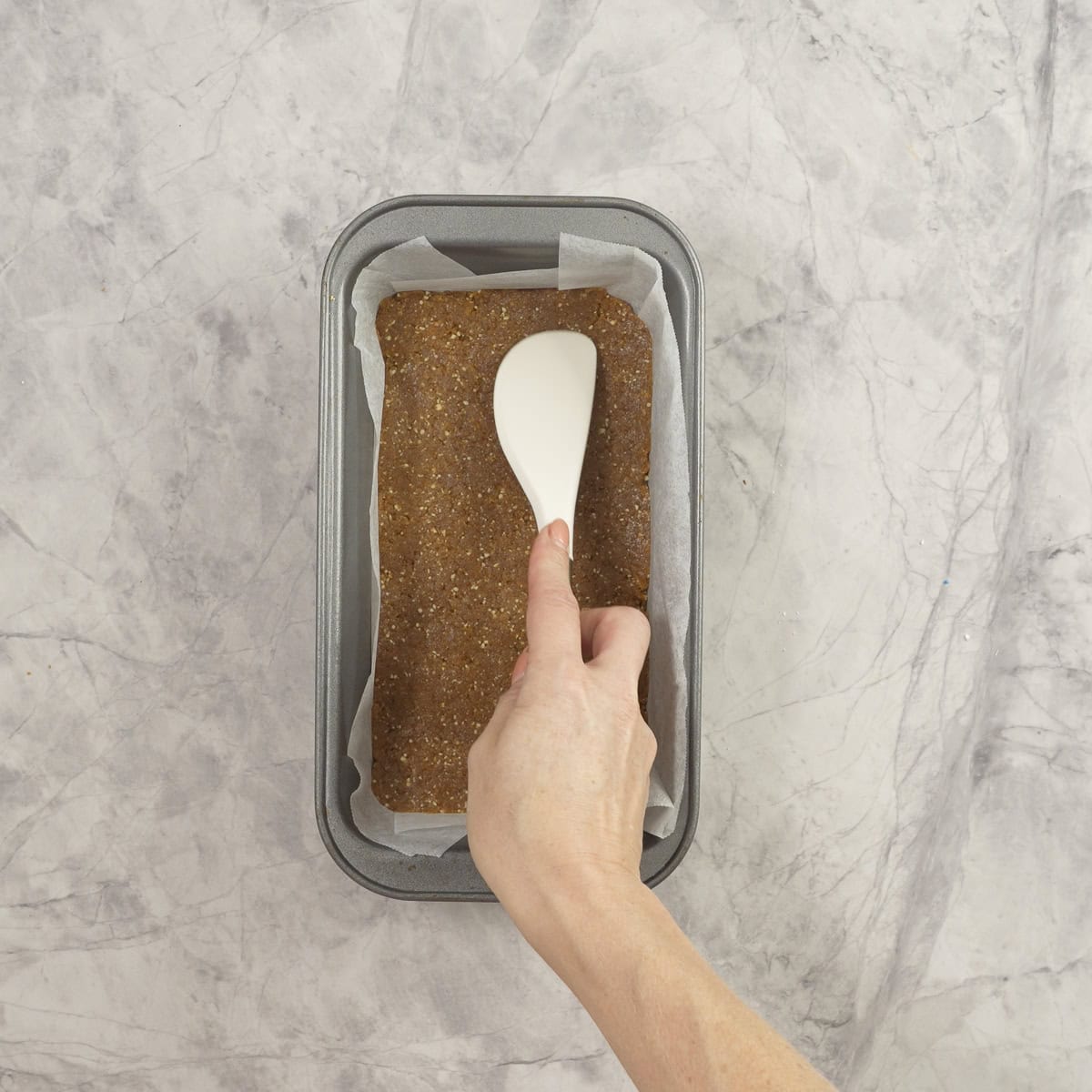 Apricot mix being pressed into a loaf tin with a spatula.