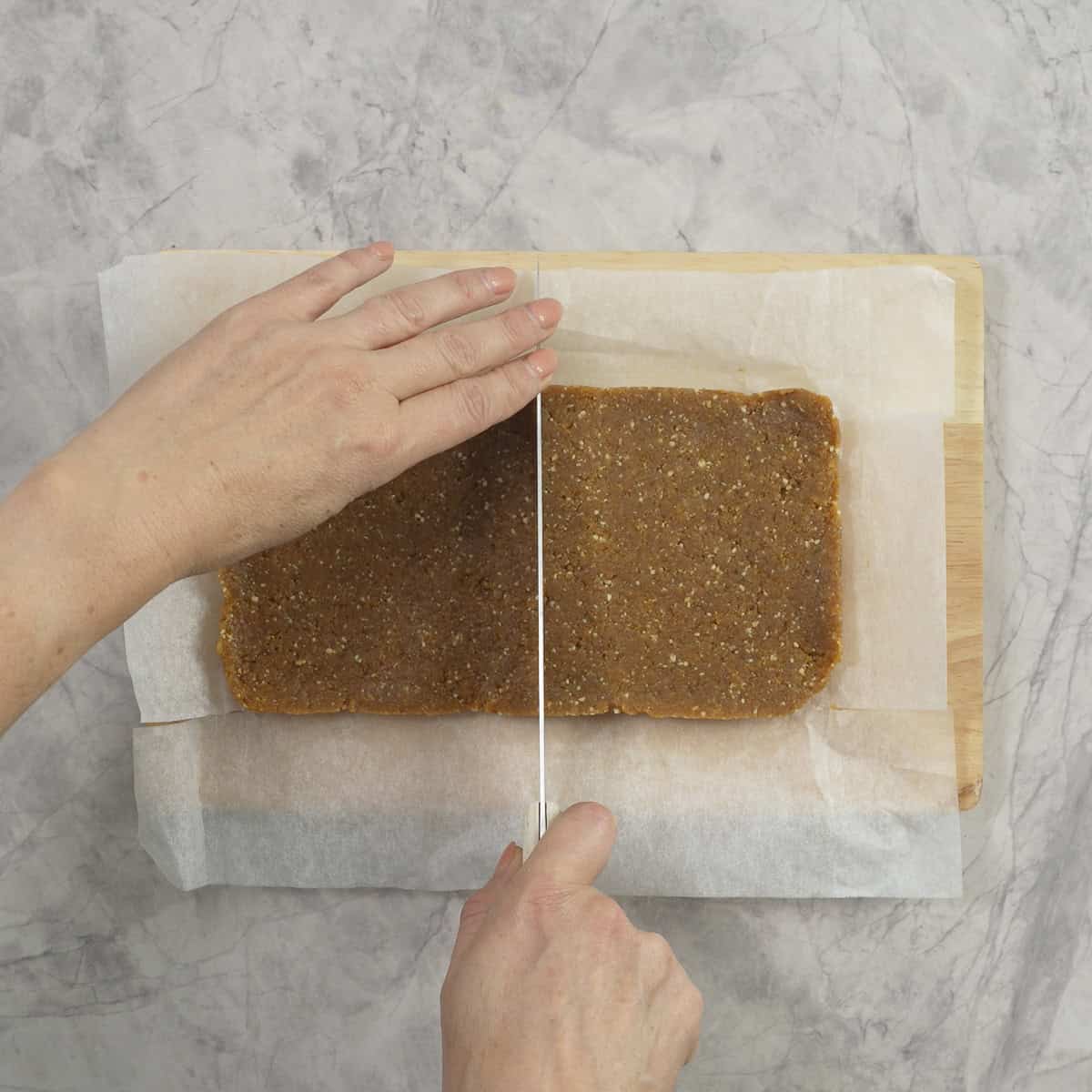 Slap of apricot mix being cut into apricot bars with a sharp knife.