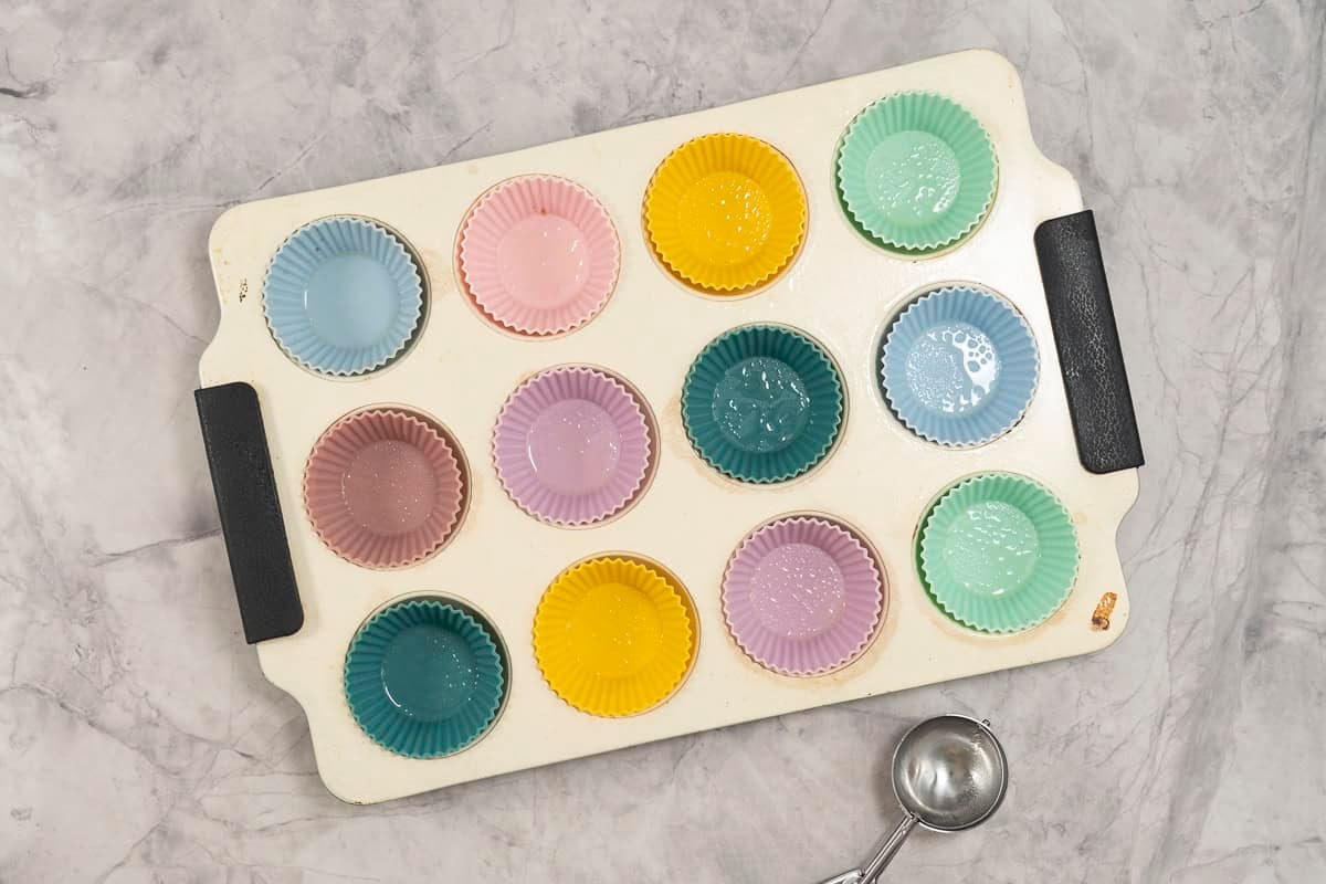 Muffin tray on bench top with colourful silicone molds inside.