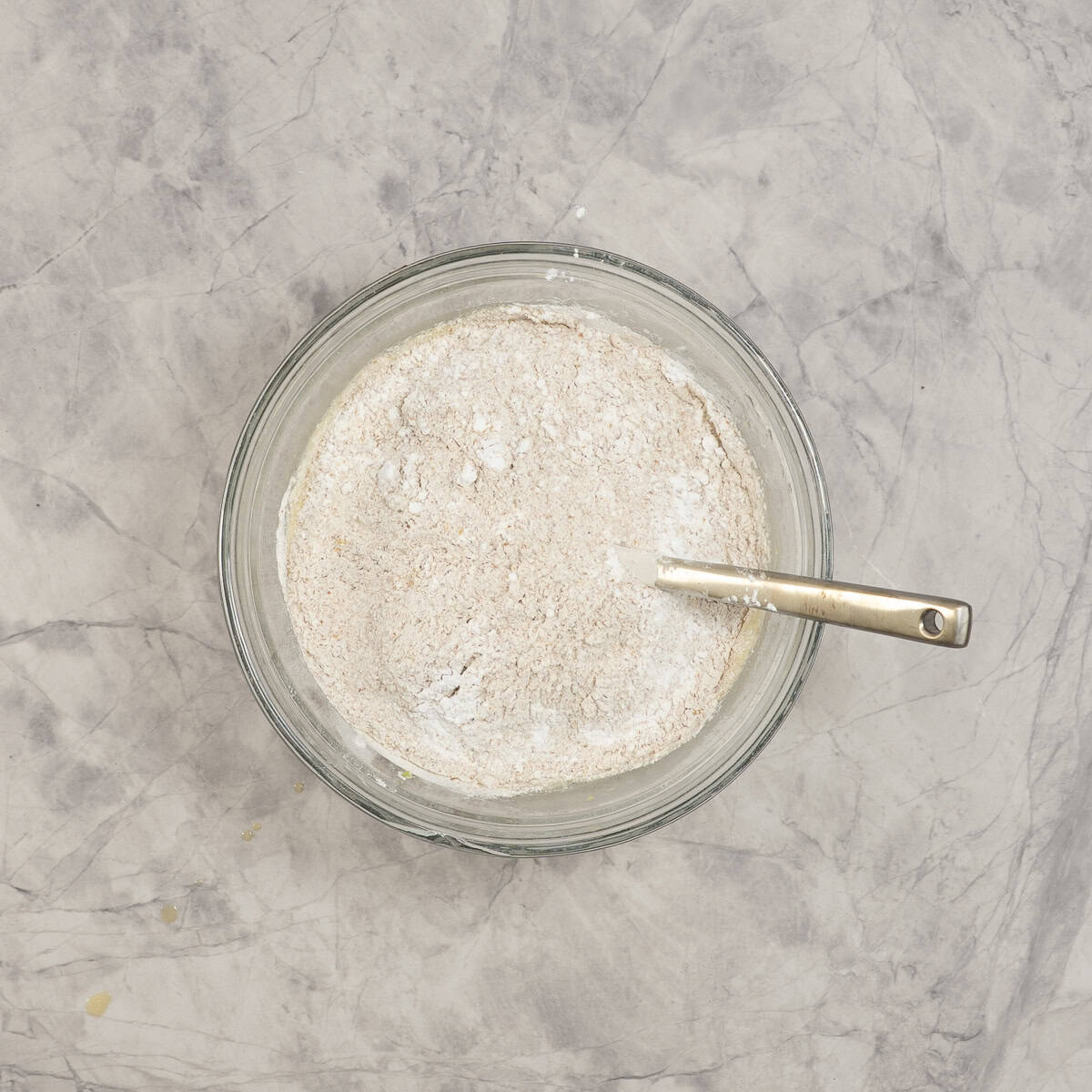Dry ingredients added into bowl of wet ingredients in glass bowl on benchtop.