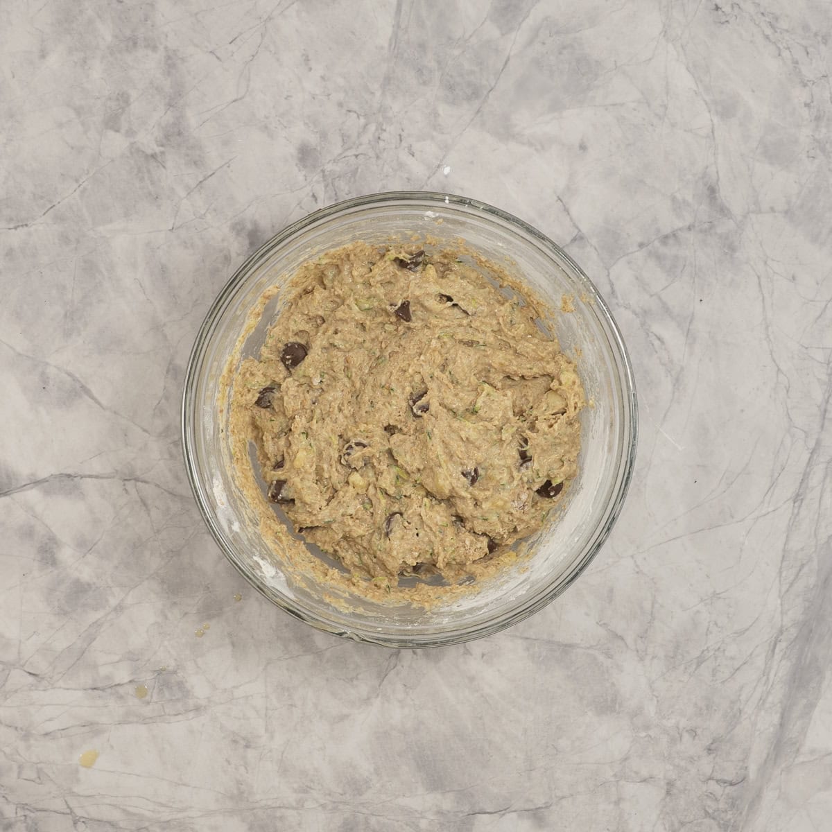 Banana zucchini batter inside large glass bowl on benchtop.