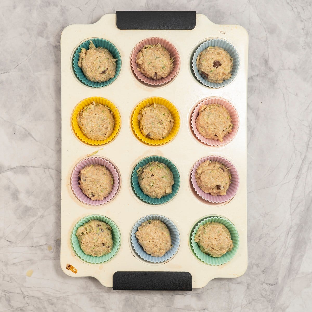 Muffin tray with colourful silicone liners muffin batter inside.