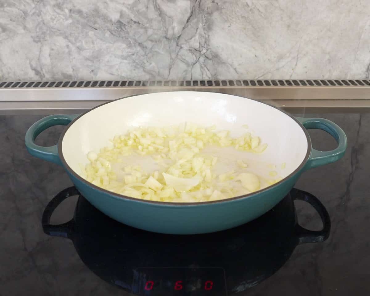 Onion sautéing in pan on stove top.