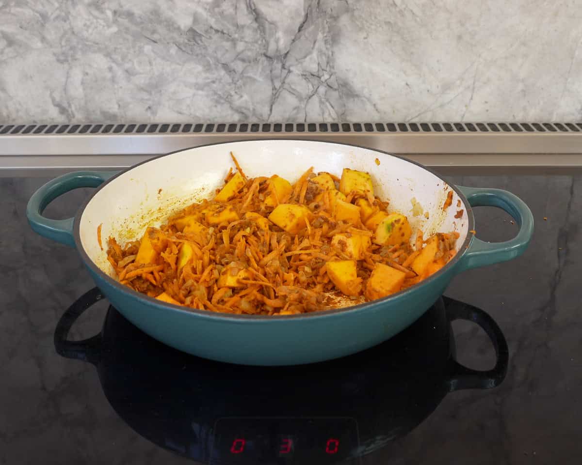 Chopped pumpkin and grated carrot added into pan with curry paste and onion.