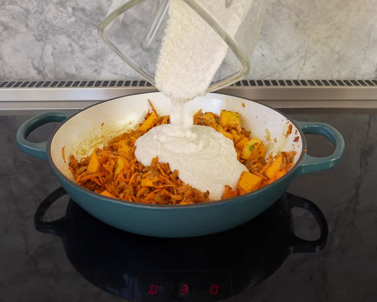 Cauliflower and coconut milk blend being poured into pan with other curry ingredients.