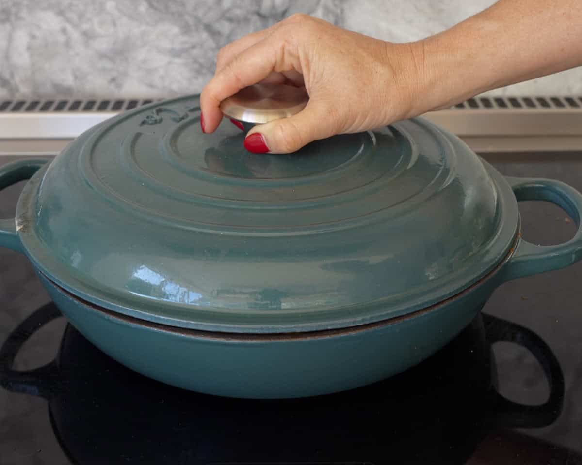 Hand putting lid on chicken curry.