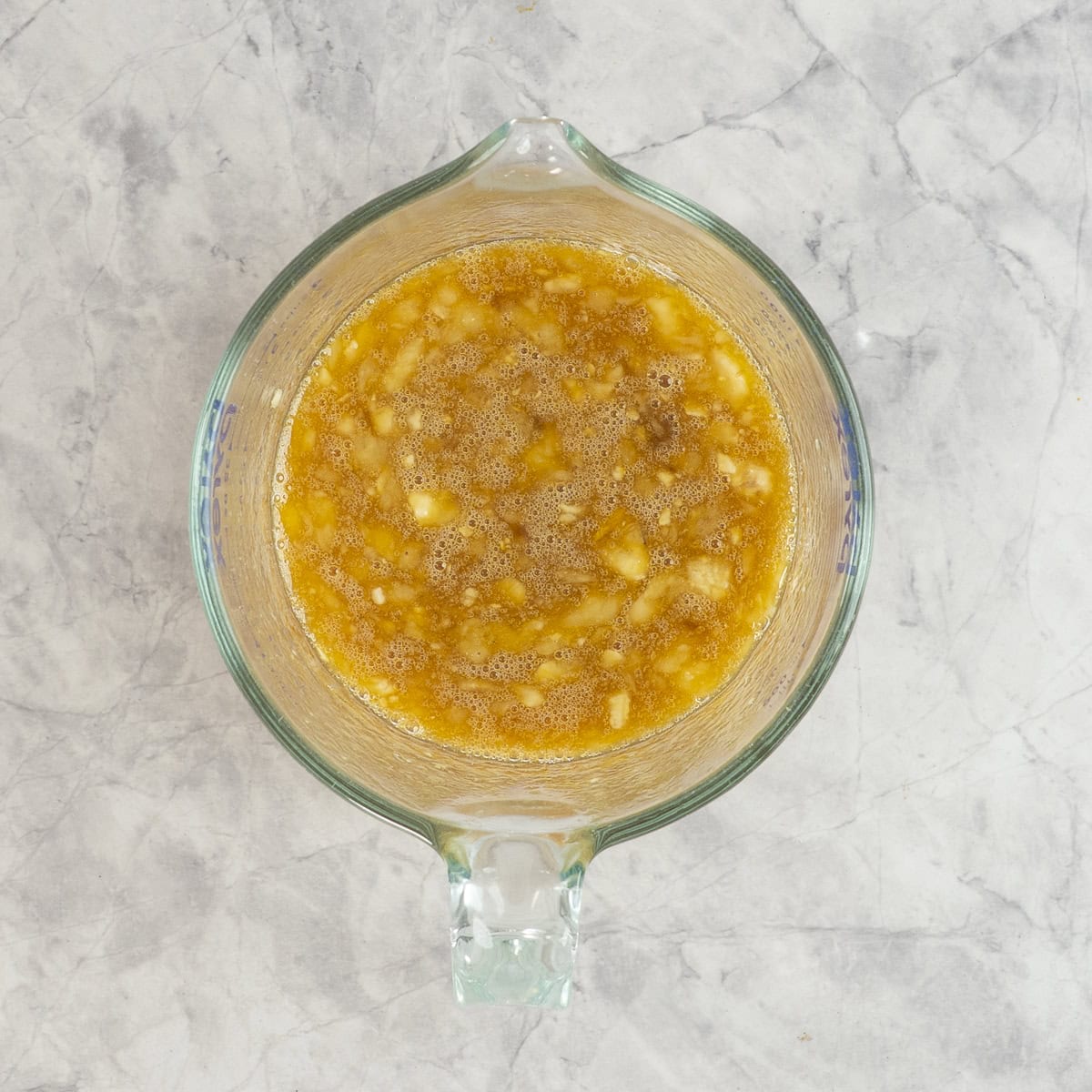 Mashed banana, eggs, oil, maple syrup, vanilla and baking soda in a glass measuring jug on betchtop.