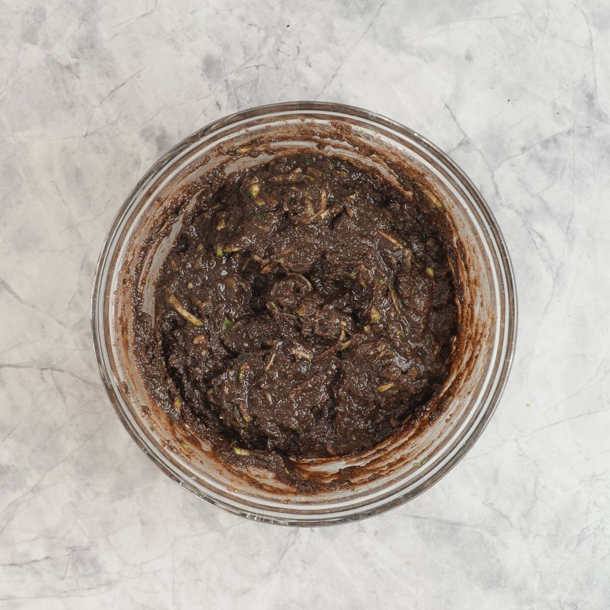 Batter for chocolate zucchini muffins in glass bowl on benchtop.